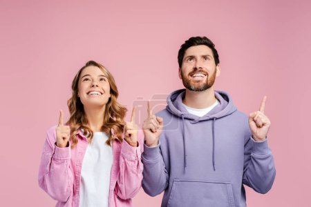 Photo for Portrait of excited, handsome man and young woman wearing stylish casual stylish clothes pointing fingers, copy space standing isolated on pink background. Shopping concept, advertisement - Royalty Free Image