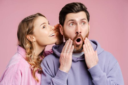 Photo for Portrait of handsome excited man looking away woman talking secret in his ear, isolated on pink background. Sale, shopping concept - Royalty Free Image