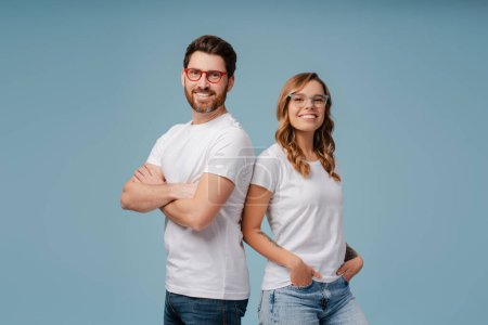 Photo for Portrait of successful smiling man and woman wearing white t shirt and stylish glasses isolated on blue background. Happy attractive fashion models with arms crossed posing for pictures in studio - Royalty Free Image