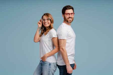 Photo for Portrait of attractive smiling man and woman wearing white t shirt and stylish eyeglasses isolated on blue background. Happy confident fashion models posing for pictures in studio - Royalty Free Image