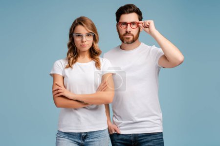 Photo for Portrait serious confident man and woman wearing white t shirt and stylish eyeglasses isolated on blue background. Attractive fashion models posing for pictures in studio - Royalty Free Image