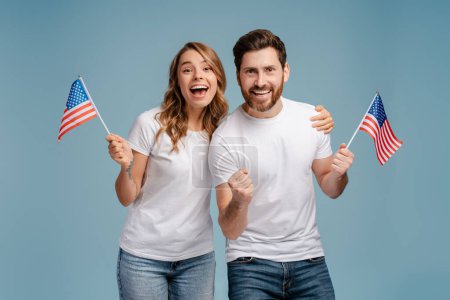 Foto de El retrato llenó de alegría a hombres y mujeres sosteniendo banderas americanas aisladas sobre fondo azul. Votación, concepto del día de las elecciones - Imagen libre de derechos