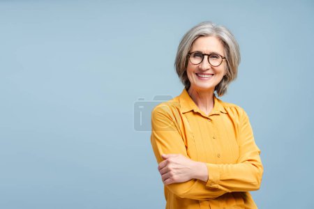 Photo for Attractive smiling business woman, manager, financier wearing eyeglasses looking away isolated on blue background. Portrait of confident gray haired CEO holding arms crossed. Successful business - Royalty Free Image