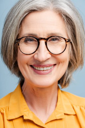 Foto de Retrato de primer plano mujer mayor sonriente con gafas con estilo mirando a la cámara aislada sobre fondo azul. Concepto de tienda óptica - Imagen libre de derechos