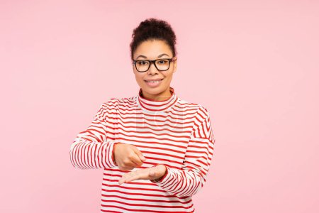 Foto de Atractiva mujer afroamericana, traductora con gafas elegantes que habla con lenguaje de señas, explicando algo mirando a la cámara aislada sobre fondo rosa. Concepto de comunicación - Imagen libre de derechos
