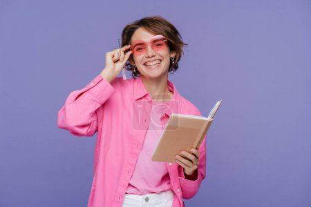 Téléchargez les photos : Étudiant souriant confiant portant des lunettes élégantes tenant livre ouvert isolé sur fond violet, concept d'éducation. Portrait belle femme heureuse, travailleur, pigiste regardant la caméra - en image libre de droit