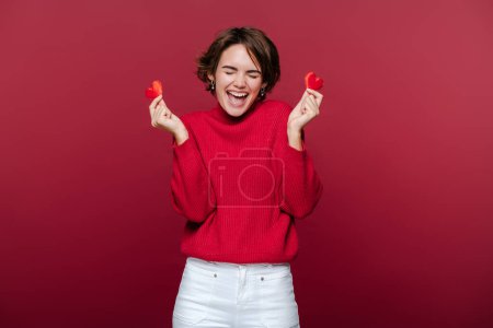 Überglücklich glückliche süße Frau mit zwei roten Herzen und schreit mit offenem Mund isoliert über roten Wand Hintergrund. Feier zum Valentinstag