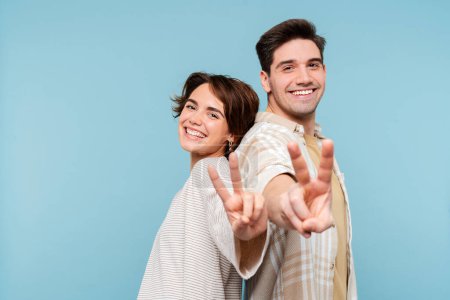 Foto de Retrato de feliz pareja sonriente haciendo un gesto, mostrando un signo de paz con los dedos mirando a la cámara aislada sobre fondo azul. Concepto de victoria - Imagen libre de derechos