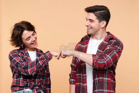 Téléchargez les photos : Portrait de couple souriant portant des chemises à carreaux cognant les poings isolés sur fond beige. Style de vie positif, concept de travail d'équipe - en image libre de droit