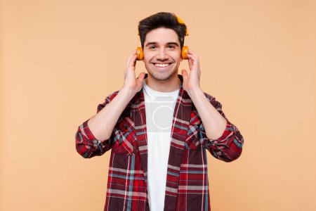 Photo for Stylish brunette man wearing headphones listening music, enjoying music isolated on beige wall background. Technologies concept - Royalty Free Image