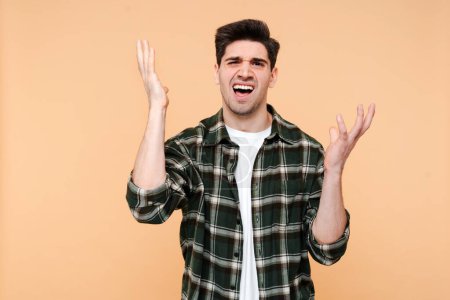 Photo for Angry stressed young man gesturing hands, screaming loud isolated on beige background. Unhappy employee fired from job - Royalty Free Image