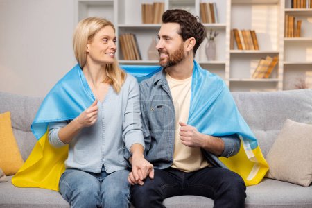 Photo for United in patriotism, a happy man and woman sit closely on their living room sofa, draped in the colors of the Ukrainian flag, showing solidarity with their country - Royalty Free Image