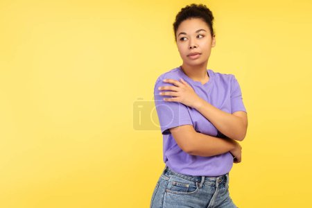 Foto de Representación de la pureza. Encantadora foto de una joven afroamericana vestida con una camiseta, salvaguardándose con las manos y evitando su mirada, aislada sobre un fondo amarillo - Imagen libre de derechos