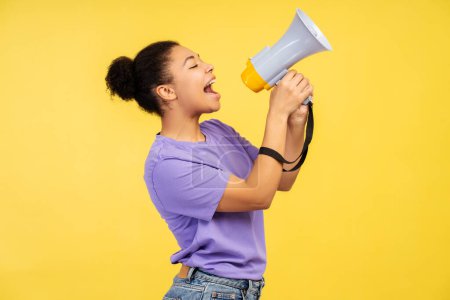 Photo for Discount news theme. Image of a beautiful young African American female in a t-shirt, screaming into a loudspeaker, on a vivid yellow background - Royalty Free Image