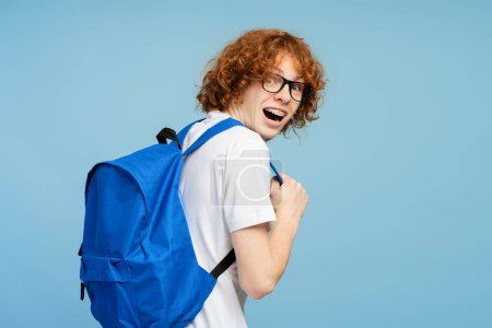 Photo for Attractive smart amazed university student with backpack looking at camera over shoulder isolated on blue background. Education concept - Royalty Free Image