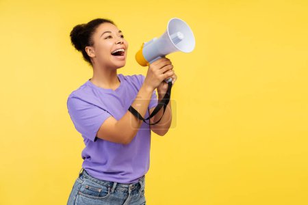 Photo for Portrait of excited smiling African American woman holding megaphone announcing, talking something, looking away on copy space standing isolated on yellow background. Concept announcement - Royalty Free Image