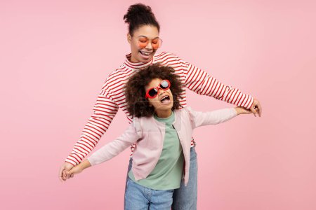 Photo for Portrait of smiling beautiful mother and little cute daughter wearing stylish sunglasses dancing isolated on pink background. Concept of fun, motherhood, childhood - Royalty Free Image