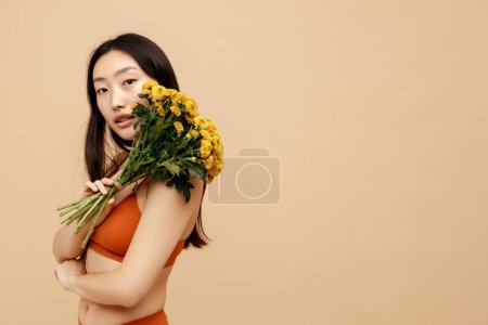 Téléchargez les photos : Portrait souriant belle femme asiatique portant une lingerie sexy tenant de belles fleurs printanières isolées sur fond, espace de copie. Modèle de mode chinois posant pour des photos. Journée internationale de la femme - en image libre de droit