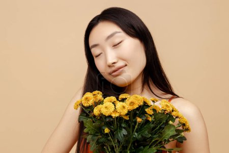 Téléchargez les photos : Joyeux attrayant asiatique femme, mariée mignonne tenant bouquet de belles fleurs jaunes isolées sur fond beige, le jour du mariage. Beauté naturelle, Printemps, Journée internationale de la femme concept - en image libre de droit