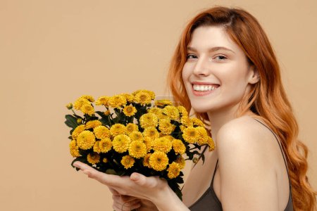 Photo for Portrait beautiful smiling cute woman holding bouquet of yellow chrysanthemums flowers looking at camera isolated on beige background. Natural beauty, spring, International women's day concept - Royalty Free Image