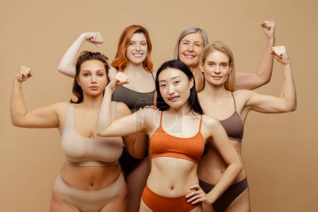 Photo for Group strong confident multiracial women wearing colorful lingerie showing muscles isolated on background. Beautiful females looking at camera. Diversity, feminism, International women's Day concept - Royalty Free Image