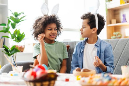 Photo for Authentic portrait happy African American kids wearing bunny ears eating tasty chocolate eggs celebration Easter at home - Royalty Free Image