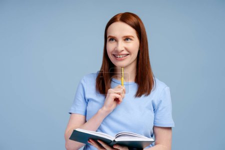 Photo for Smart pondering school woman holding book and pen isolated on blue background. College student studying, learning language. Education concept - Royalty Free Image