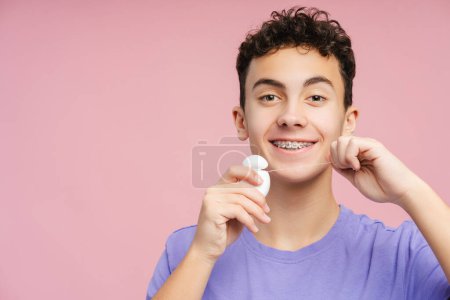 Foto de Adolescente sonriente con aparatos ortopédicos, dientes cuidadosamente hilo dental, aislado sobre fondo rosa. Subraya la importancia del mantenimiento dental - Imagen libre de derechos