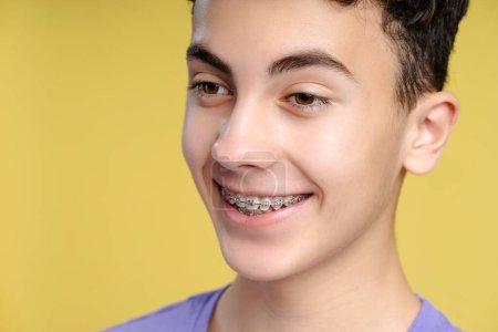 Foto de Retrato de primer plano de un niño sonriente y confiado con aparatos dentales en los dientes mirando hacia otro lado, aislado sobre un fondo amarillo. Salud, concepto de ortodoncia - Imagen libre de derechos