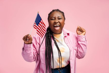 Foto de Retrato feliz mujer afroamericana con estilo, partidario con bandera de EE.UU., a la espera de resultado de las elecciones presidenciales aislado en el fondo rosa. Votación, libertad, concepto electoral - Imagen libre de derechos