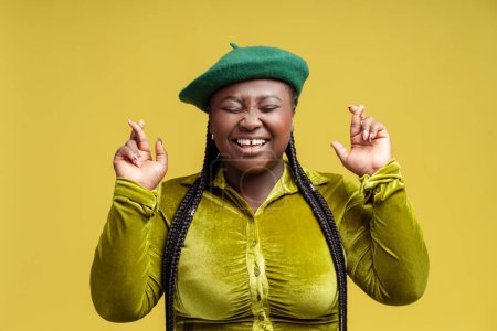 Téléchargez les photos : Femme afro-américaine drôle élégant tenant les doigts croisés souhaitent quelque chose d'isolé sur fond vert. Espoir, concept publicitaire - en image libre de droit