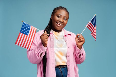 Photo for Portrait smiling African American woman holding American flags isolated on blue background. Voting, election concept - Royalty Free Image