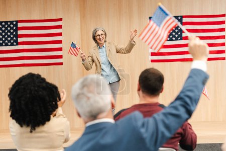 Portrait of smiling confident woman, politician, presidential candidate holding American flag communication, speaking with audience. Vote, United States presidential election concept 