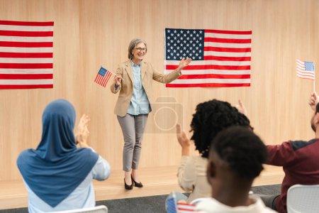 Attraktive selbstbewusste Seniorin, Politikerin, Präsidentschaftskandidatin mit amerikanischer Flagge, die eine Rede hält und die Menge applaudiert. Vote, Wahlkampfkonzept für US-Präsidentschaftswahlen 