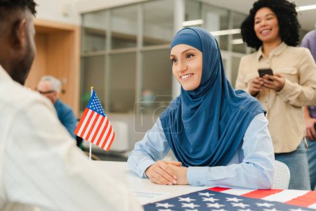 Téléchargez les photos : Une femme souriante portant le hijab attend l'inscription des électeurs au bureau de vote. Démocratie, vote, concept d'élection présidentielle américaine - en image libre de droit