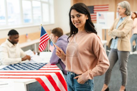 Photo for Portrait of smiling woman, voter holding American flag waiting in line at polling station. Democracy, freedom, vote, United States presidential election concept - Royalty Free Image