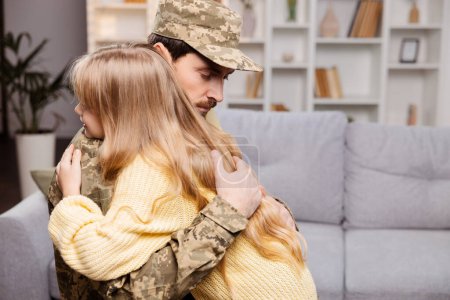 Téléchargez les photos : Heureuse famille qui profite d'une réunion militaire. Papa en uniforme, embrassant sa fille heureuse dans leur salon confortable - en image libre de droit