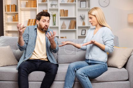 Escena de conflicto. Un hombre y una mujer gesticulando activamente durante una discusión. Sentados juntos en el sofá de la sala