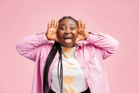 Foto de Hermosa, sonriente mujer afroamericana llena de alegría gritando algo, vistiendo ropa casual con estilo, mirando a la cámara. Mujer joven y feliz aislada sobre fondo rosa. Concepto de estilo de vida positivo - Imagen libre de derechos