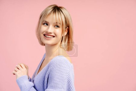 Téléchargez les photos : Portrait mignon heureux confiant jeune femme avec des appareils dentaires sur les dents regardant loin isolé sur fond rose, espace de copie. Soins de santé, traitement, concept orthodontique - en image libre de droit