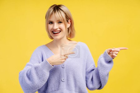 Photo for Portrait of happy smiling blonde haired woman wearing stylish casual clothes pointing fingers on copy space isolated on yellow background. Shopping, sale concept - Royalty Free Image