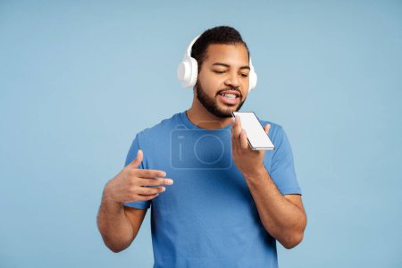 Photo for Smiling bearded man in headphones, wearing teeth braces calling mobile phone, isolated on a blue background. Technologies and people concept - Royalty Free Image