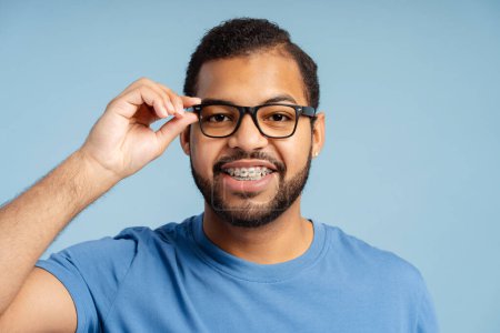 Photo for Portrait of smiling smart african american man with braces wearing glasses isolated on blue background. Education concept - Royalty Free Image