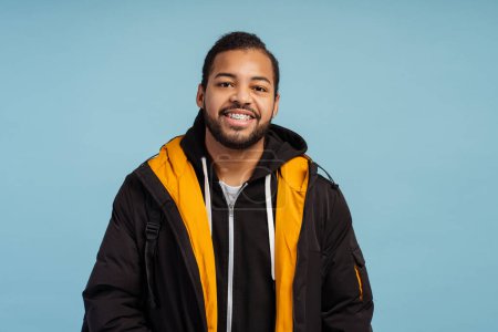 Photo for Portrait of positive happy man with braces looking at camera, wearing winter jacket standing isolated over blue background. Advertisement concept, dental care - Royalty Free Image