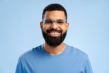 Photo for Attractive, smiling, bearded African American man wearing stylish eyeglasses looking at camera standing isolated on blue background. Vision concept, treatment - Royalty Free Image
