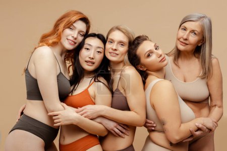 Photo for Group of multiracial, diverse, beautiful women wearing sexy lingerie, looking at camera, hugging. Beautiful, sensual fashion models posing isolated on beige background. Concept of femininity - Royalty Free Image