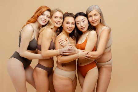 Foto de Hermosa sonrisa diversas mujeres multiétnicas con estilo sexy lencería abrazos mirando a la cámara, modelos de moda posando aislados sobre fondo beige. Concepto del Día Internacional de la Mujer - Imagen libre de derechos