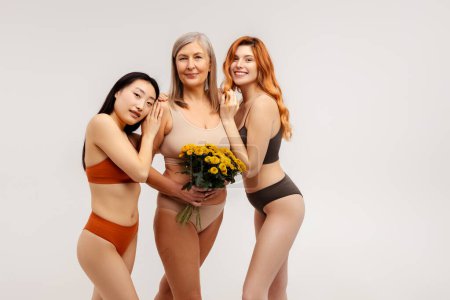 Photo for Group of multiracial asian, red hair and senior women, holding bunch of chrysanthemums wearing lingerie looking at camera standing isolated on white background, copy space. Diversity concept - Royalty Free Image