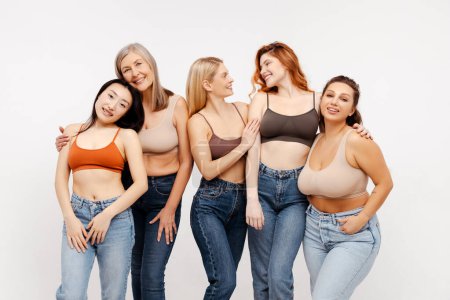 Photo for Group of smiling beautiful women friends hugging, wearing sexy bras and jeans. Attractive different fashion models posing isolated on white background. Diverse concept, international women's day - Royalty Free Image