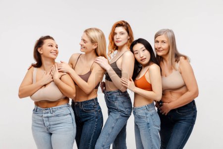 Foto de Grupo de mujeres multirraciales diversas elegantes que usan sujetadores sexy y jeans abrazando hablando mirando a la cámara aislada en el fondo blanco. Hermosas modelos de moda posando en ropa interior. Concepto de apoyo - Imagen libre de derechos